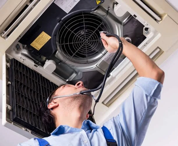 Technician inspecting the fan assembly of a ceiling-mounted HVAC unit