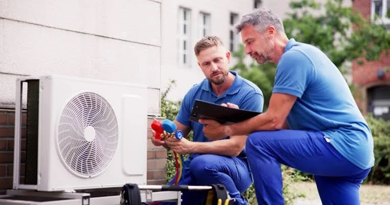 Two HVAC technicians assessing an outdoor system with gauges and a tablet